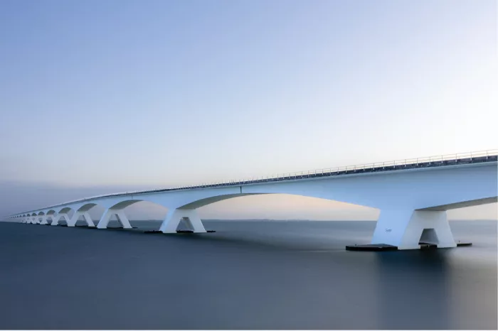 Witte bogen van de Zeelandbrug boven spiegelglad water in blauw en roze schemerlicht