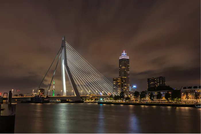 Verlichte Erasmusbrug en skyline van Rotterdam bij nacht, met lichtreflecties in de rivier