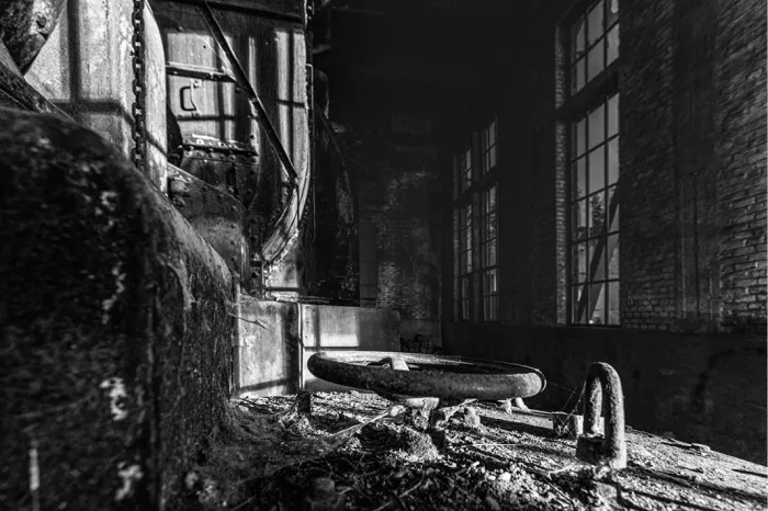 Verlaten machinehal van de oude elektriciteitscentrale Transfo in Zwevegem, met roestige machines, een groot handwiel en licht dat door hoge vensters valt.