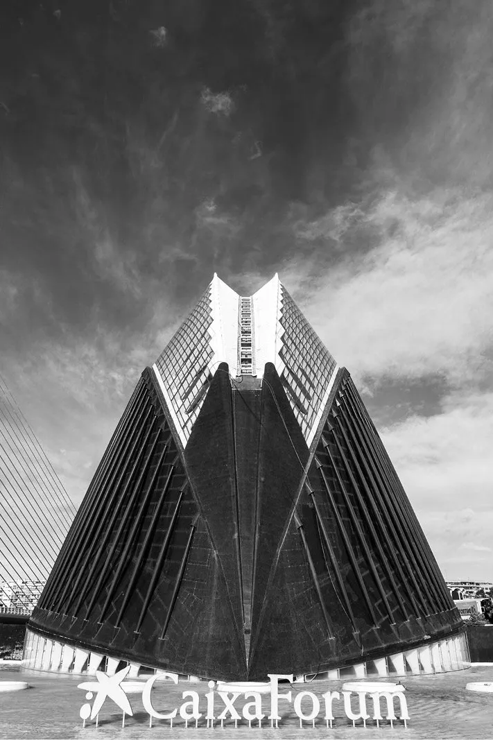 Symmetrische gevel met scherpe, waaiervormige ribben in de Ciutat de les Arts i les Ciències in Valencia, met het opschrift CaixaForum op de voorgrond.