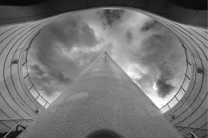 Blik omhoog door een ronde opening in de witte architectuur van de Ciutat de les Arts i les Ciències in Valencia, met een puntige constructie tegen een dramatische wolkenlucht.