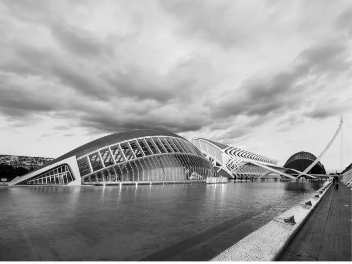 Futuristische gebouwen van de Ciutat de les Arts i les Ciències in Valencia weerspiegelen in een lange vijver onder een zware wolkenlucht.