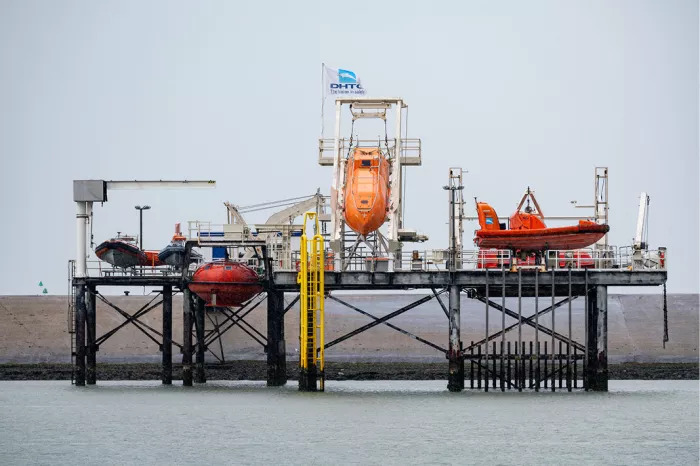Oefenplatform op palen in het water met oranje reddingsboten, kranen en gele trappen
