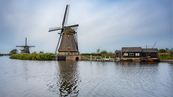 Windmolens en een molenaarshuis aan het water, met een molen die in het water spiegelt