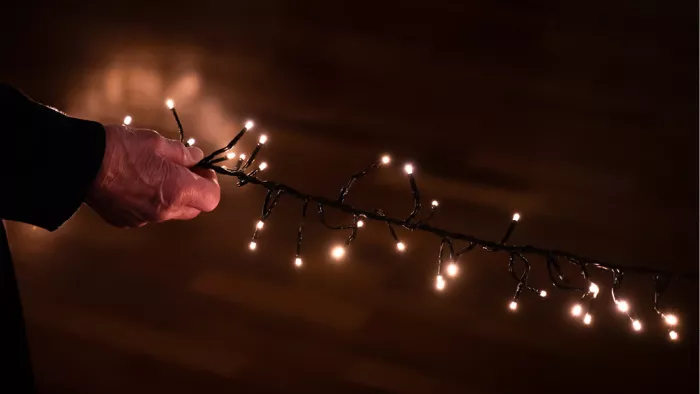 Oude hand houdt een snoer met warme lichtjes vast tegen een donkere achtergrond