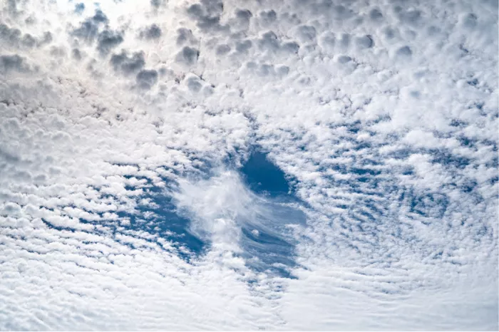 Veld van kleine schapenwolkjes met een gat waarin blauwe lucht en een ijspluim zichtbaar zijn