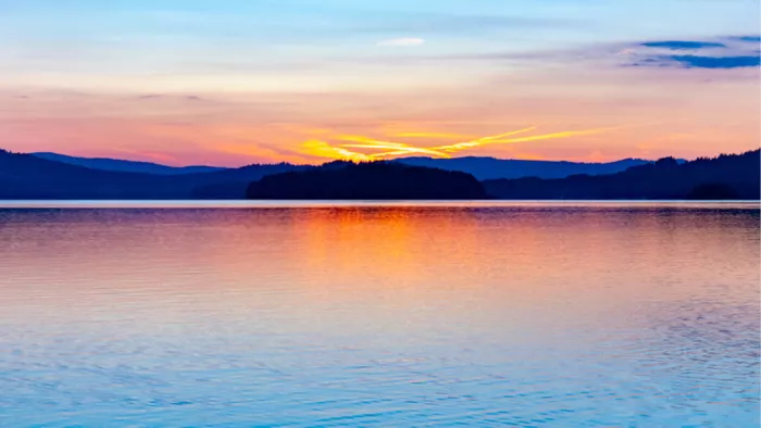 Oranje en roze zonsondergang boven blauwe heuvels, gespiegeld in een kalm meer