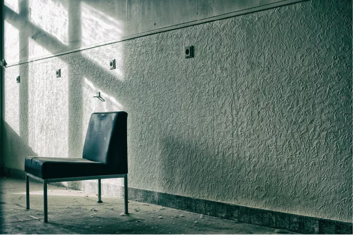 Zwarte vintage zetel in een verlaten ruimte, naast een muur met reliëfbehang waarop licht en schaduw van een raam vallen
