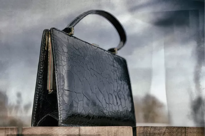 Zwarte vintage handtas van krokodillenleer op een houten plank tegen een grijze wolkenlucht, lage camerahoek