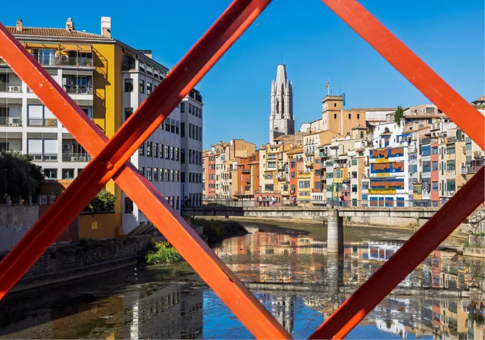 Kleurrijke huizen en kerktoren van Girona langs de rivier, gezien door het rode vakwerk van de Eiffelbrug