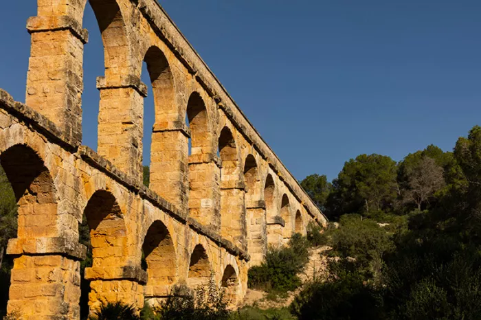 Romeins aquaduct met een rij stenen bogen in warm avondlicht tegen een diepblauwe lucht