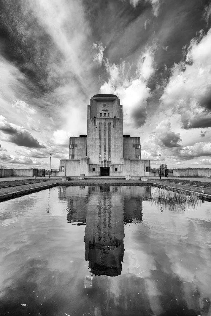Symmetrisch radiogebouw met spiegelbeeld in een vijver, onder uitwaaierende wolken