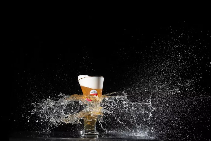 Bierglas wordt door een kogel doorboord, met bier en druppels die opzij spatten tegen een zwarte achtergrond