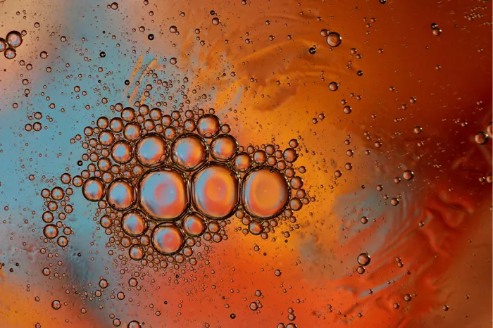 Oliedruppels op water in oranje, rood en lichtblauw, met een tros grote bellen in het midden