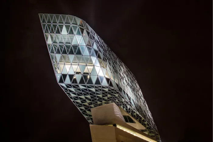 Glazen uitbouw met driehoekige ruiten in de vorm van een diamant, verlicht tegen een zwarte nachthemel