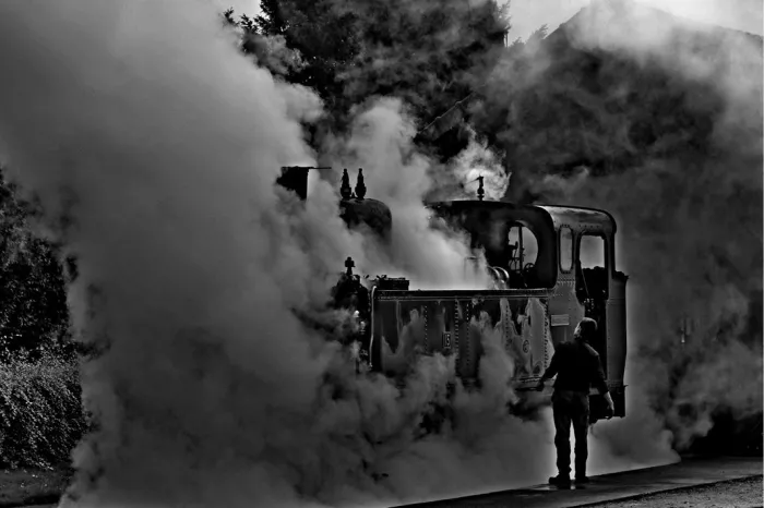 Stoomlocomotief in dichte stoomwolken met een man in silhouet ernaast
