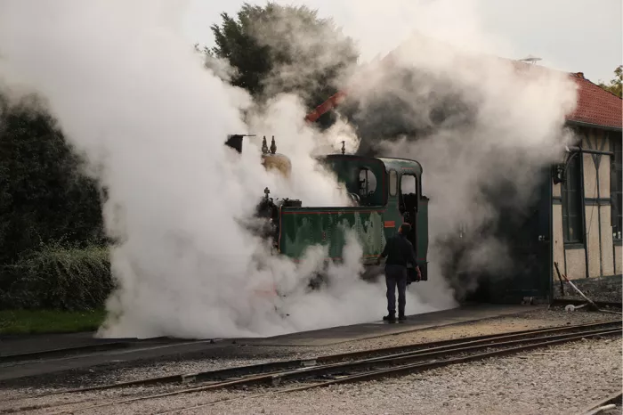 Groene stoomlocomotief onder stoom bij een stationsgebouw met rood dak