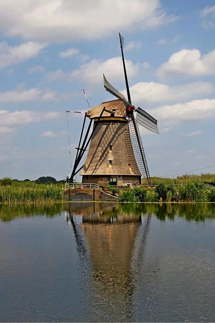 Rieten windmolen weerspiegelt in stil water onder een blauwe lucht met witte wolken