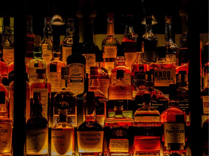 Rekken vol whiskeyflessen in warm oranje licht achter donkere spijlen