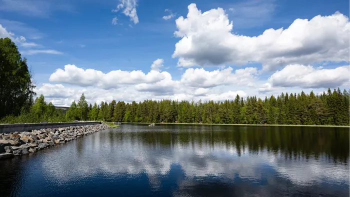 Witte wolken en sparren spiegelen in een meer met een dam van rotsblokken