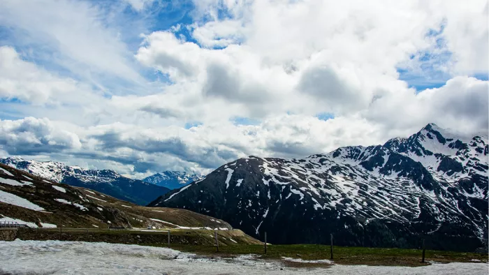 Bergpas met besneeuwde toppen en sneeuwplekken onder een wolkenlucht