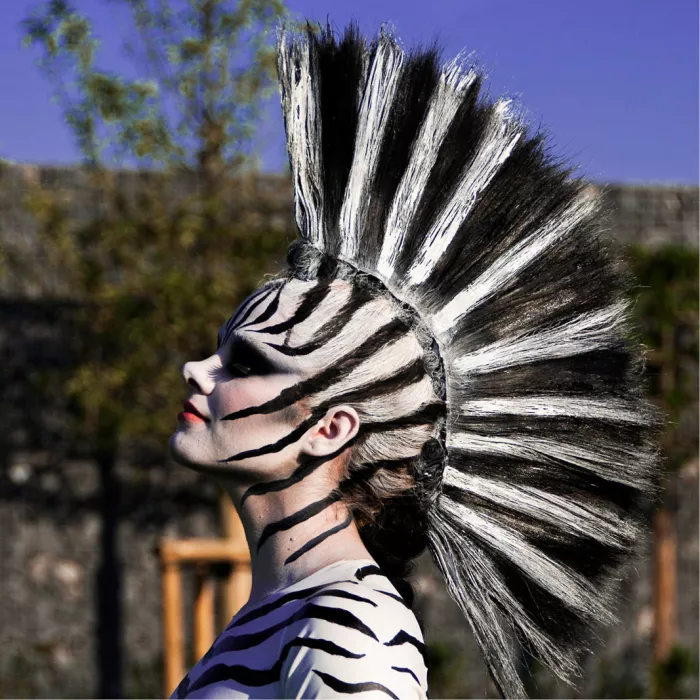 Vrouw geschminkt als zebra met zwart-witte strepen en een hoge hanenkam