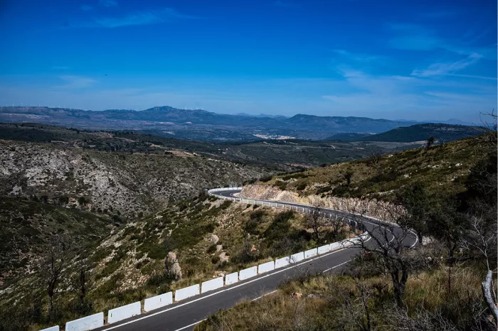 Bergweg met witte vangrails slingert langs een helling met bergen in de verte