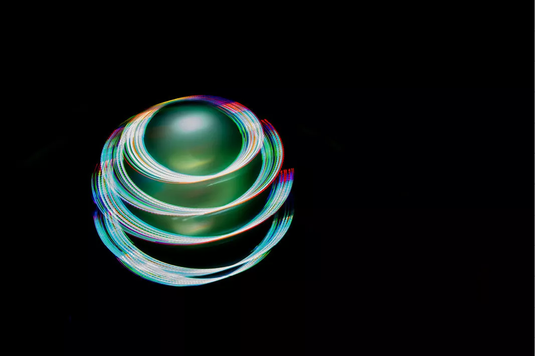 Gloeiende bol van ronddraaiende lichtsporen in regenboogkleuren tegen een zwarte achtergrond
