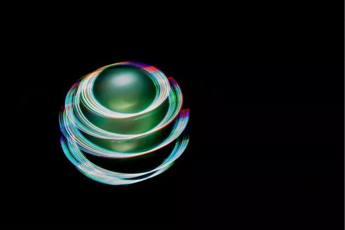 Gloeiende bol van ronddraaiende lichtsporen in regenboogkleuren tegen een zwarte achtergrond