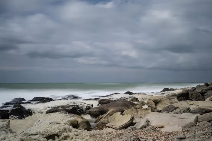 Golven breken over donkere rotsen langs de kust onder een grijze wolkenlucht