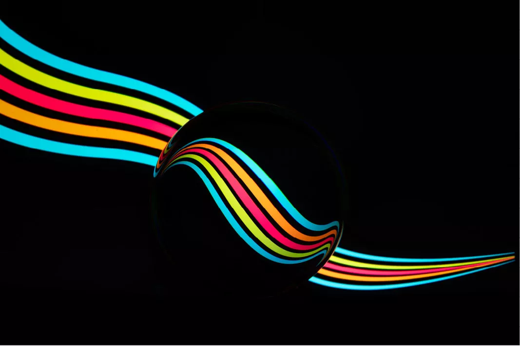 Gekleurde lichtsporen in regenboogkleuren buigen door een glazen bol tegen een zwarte achtergrond