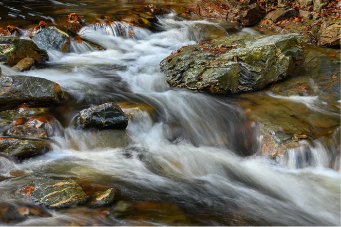 Beek met kleine watervallen tussen bemoste rotsblokken, met zacht wit water