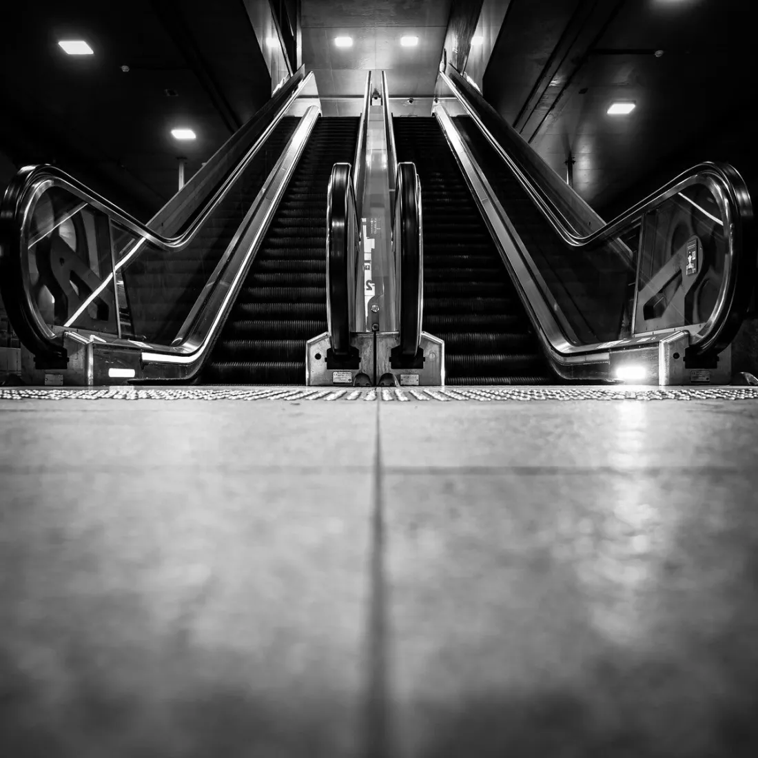 Twee lege roltrappen in station Antwerpen Centraal, laag gezien vanaf de tegelvloer, in zwart-wit.