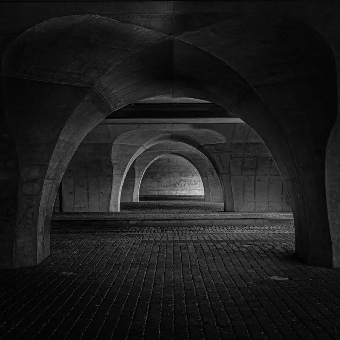 Onderdoorgang met betonnen bogen die achter elkaar in de diepte verdwijnen, boven een vloer van donkere kasseien.