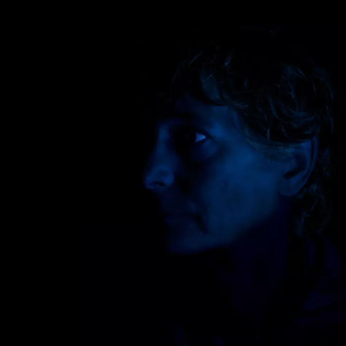 Portret in profiel van een persoon met kort, woelig haar, enkel verlicht in blauw licht tegen een zwarte achtergrond.