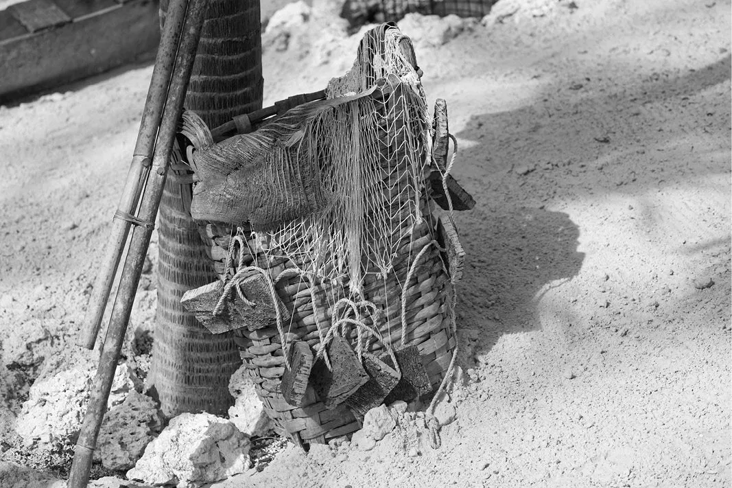 Gevlochten visfuik met touwtjes tegen een paal op zand, met bamboestokken ernaast