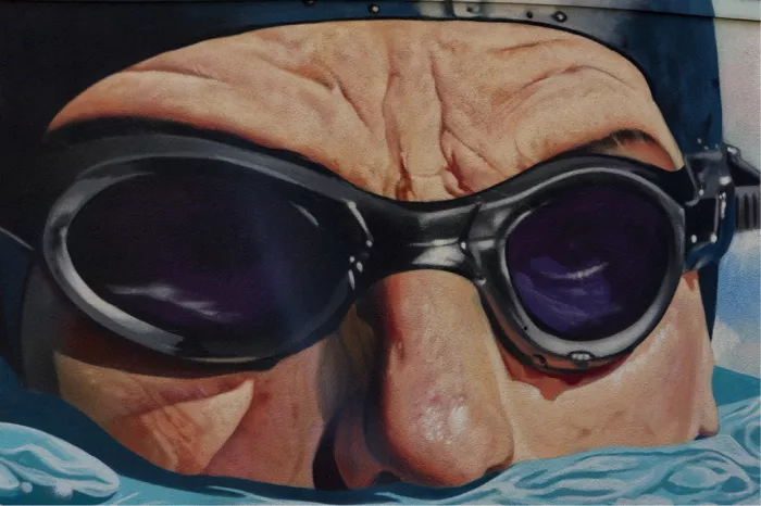 Muurschildering van een zwemmer met badmuts en zwembril net boven het water