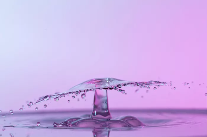 Laag waterscherm met wegspattende druppeltjes boven een waterzuil, in roze en lila tinten