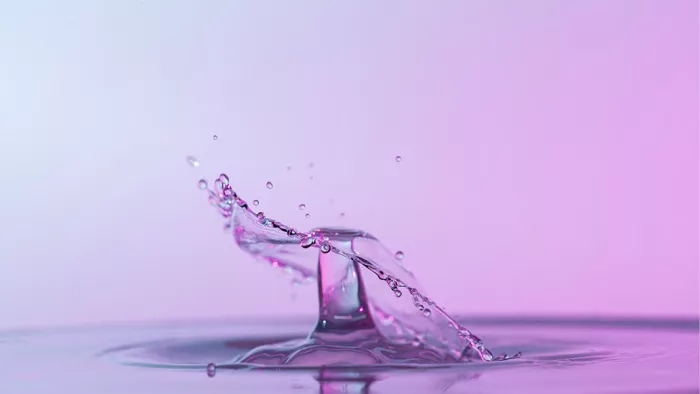 Gedraaide waaier van opspattend water na de botsing van twee druppels, tegen een roze achtergrond