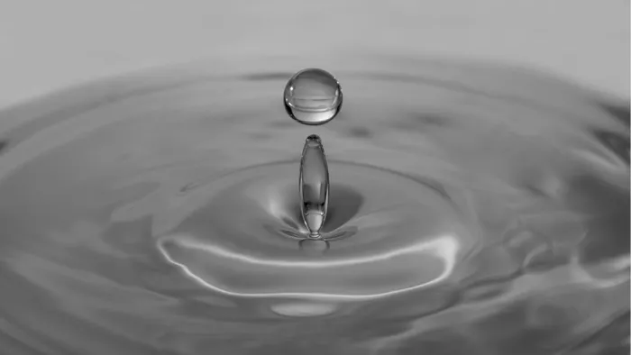 Druppel die boven een smalle waterzuil zweeft als het puntje op de i, met kringen in grijs water