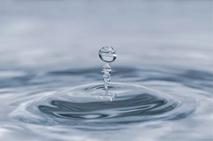 Druppel bovenop een kronkelende waterzuil met kringen in het water, in blauwe tinten