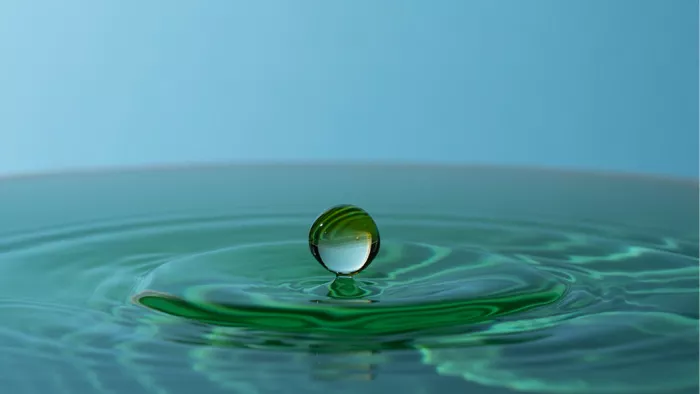 Ronde waterdruppel die boven groenblauw water zweeft, met kringen eronder