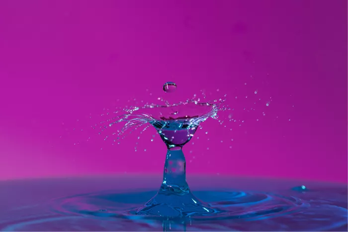 Blauwe waterzuil met een open kelk en zwevende druppel, tegen een magenta achtergrond