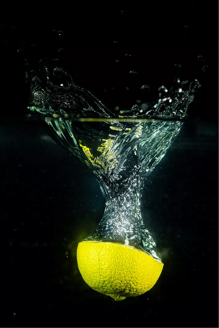 Halve gele citrusvrucht die in het water valt met een trechter van luchtbellen, tegen een zwarte achtergrond
