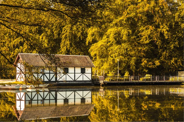 Wit vakwerk boothuisje aan een vijver met herfstbomen in geelgroen en reflectie in het water