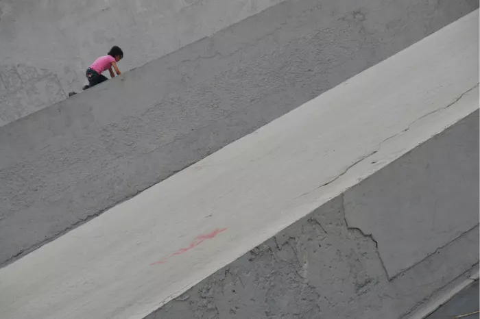 Kind in roze T-shirt klimt op een schuine grijze betonwand
