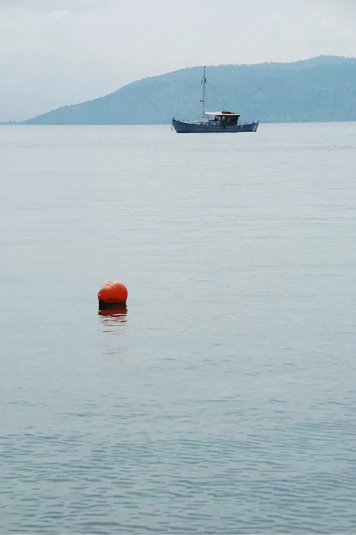 Boot op stil lichtblauw water met een heuvel erachter en een oranje boei vooraan