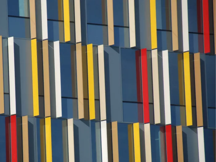 Gevel met verticale lamellen in geel, rood en wit voor donkerblauw glas