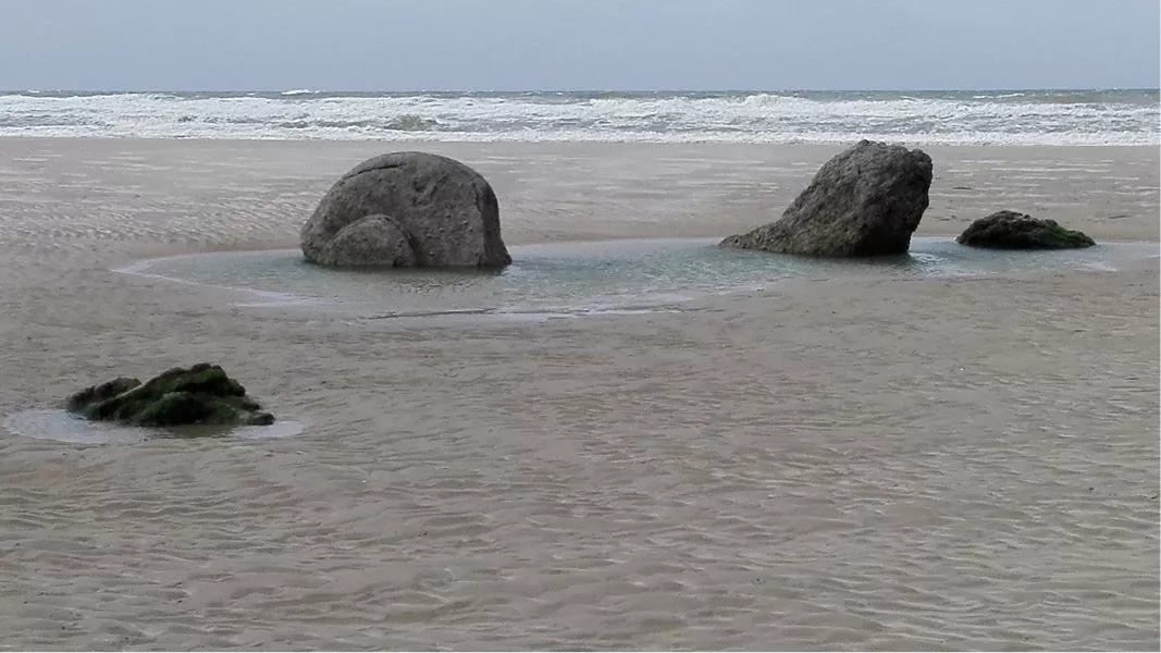 Grote rotsblokken op een nat strand met golven op de achtergrond