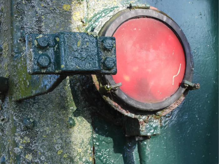 Rond rood licht op verweerd groen metaal van een oude trein, met scharnier en bouten